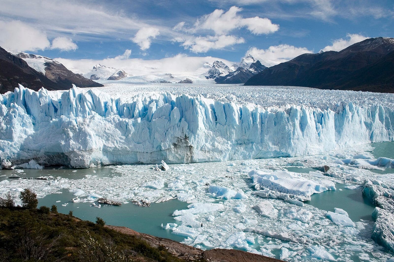 El frente del glaciar Perito Moreno sobre el lago, con témpanos y montañas nevadas